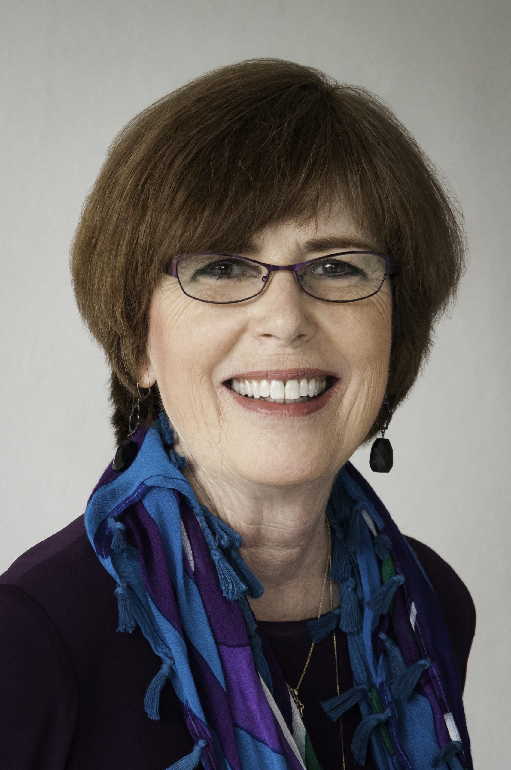 A woman with glasses and a scarf around her neck.