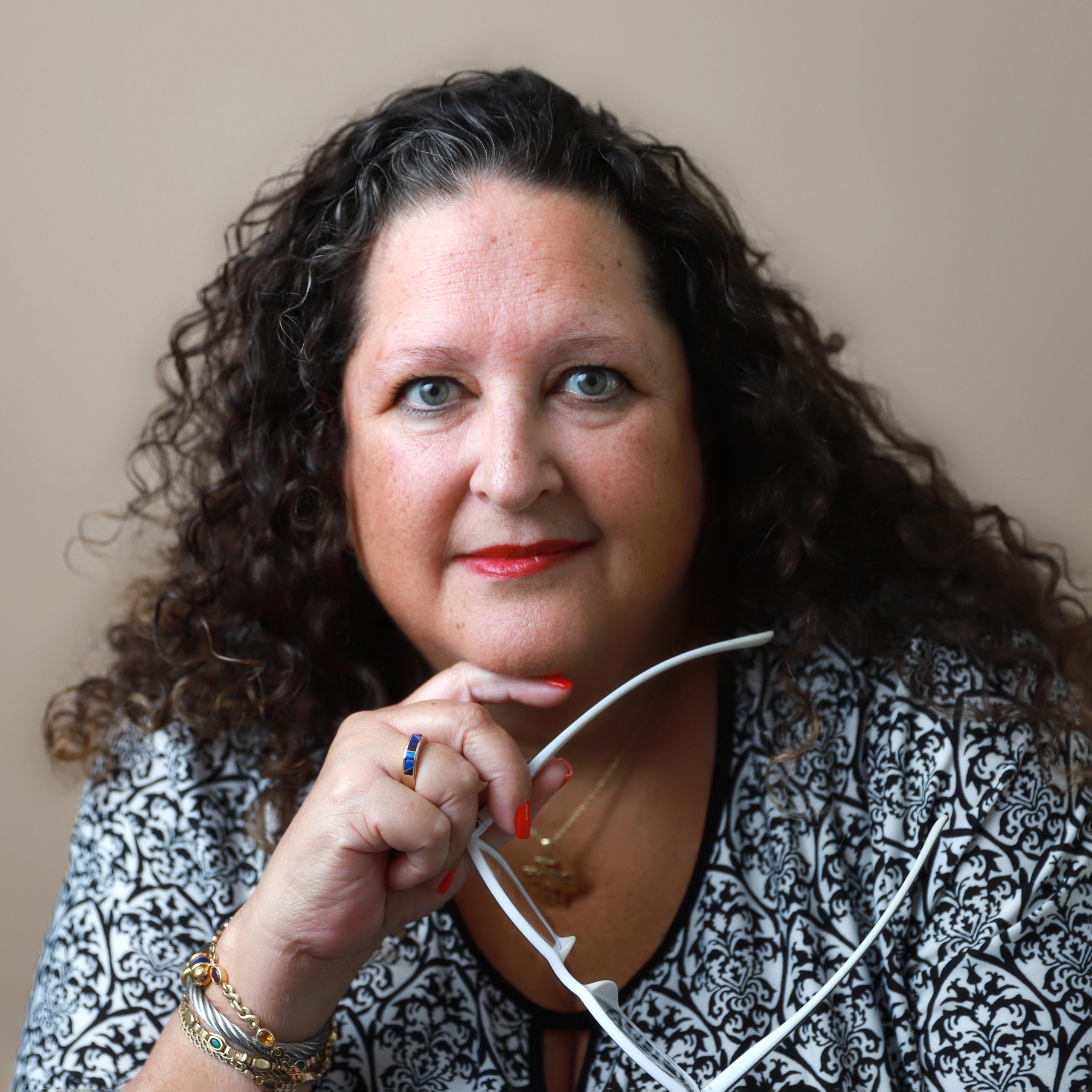 A woman with curly hair holding her glasses.